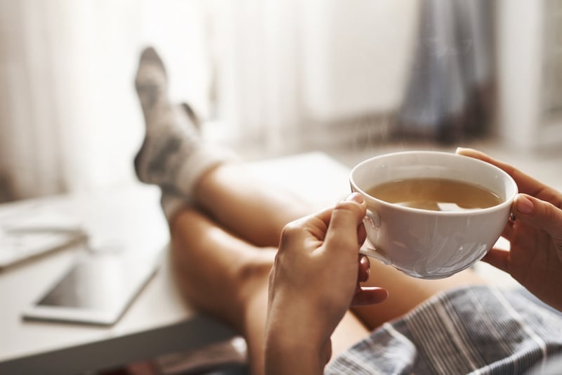 cup-of-tea-and-chill-woman-lying-on-couch-holding-legs-on-coffee-table-drinking-hot-coffee-and-enjoying-morning-being-in-dreamy-and-relaxed-mood-girl-in-oversized-shirt-takes-break-at-home