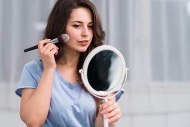 young-brunette-woman-with-makeup-brush-looking-mirror